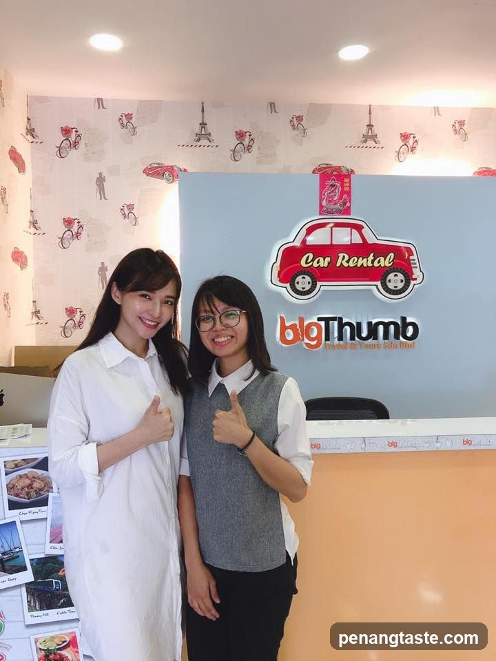 Two women giving thumbs up in front of a car rental sign