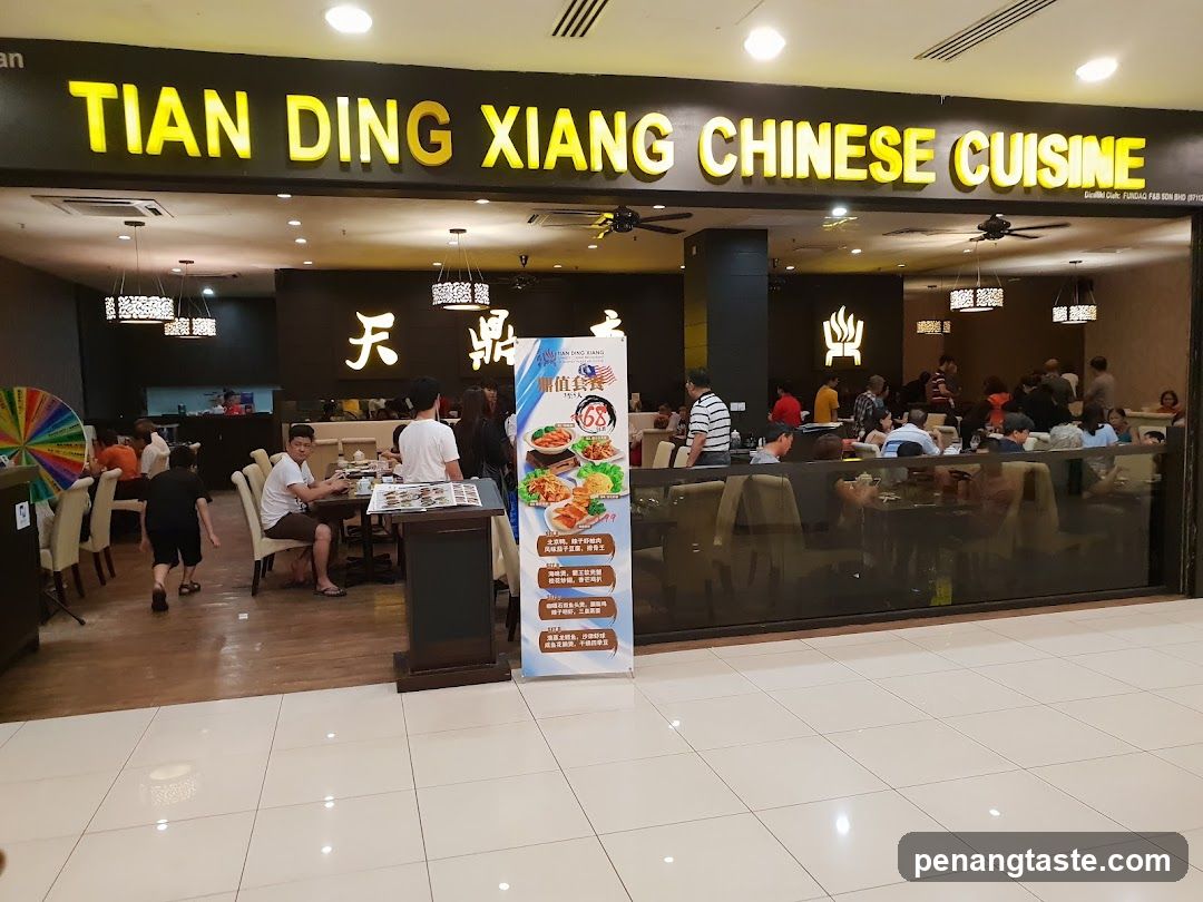 The exterior of a Chinese restaurant with a large illuminated sign that reads "TIAN DING XIANG CHINESE CUISINE". Inside, patrons are seated at tables, and staff are visible. A promotional stand with food images and text is placed near the entrance.