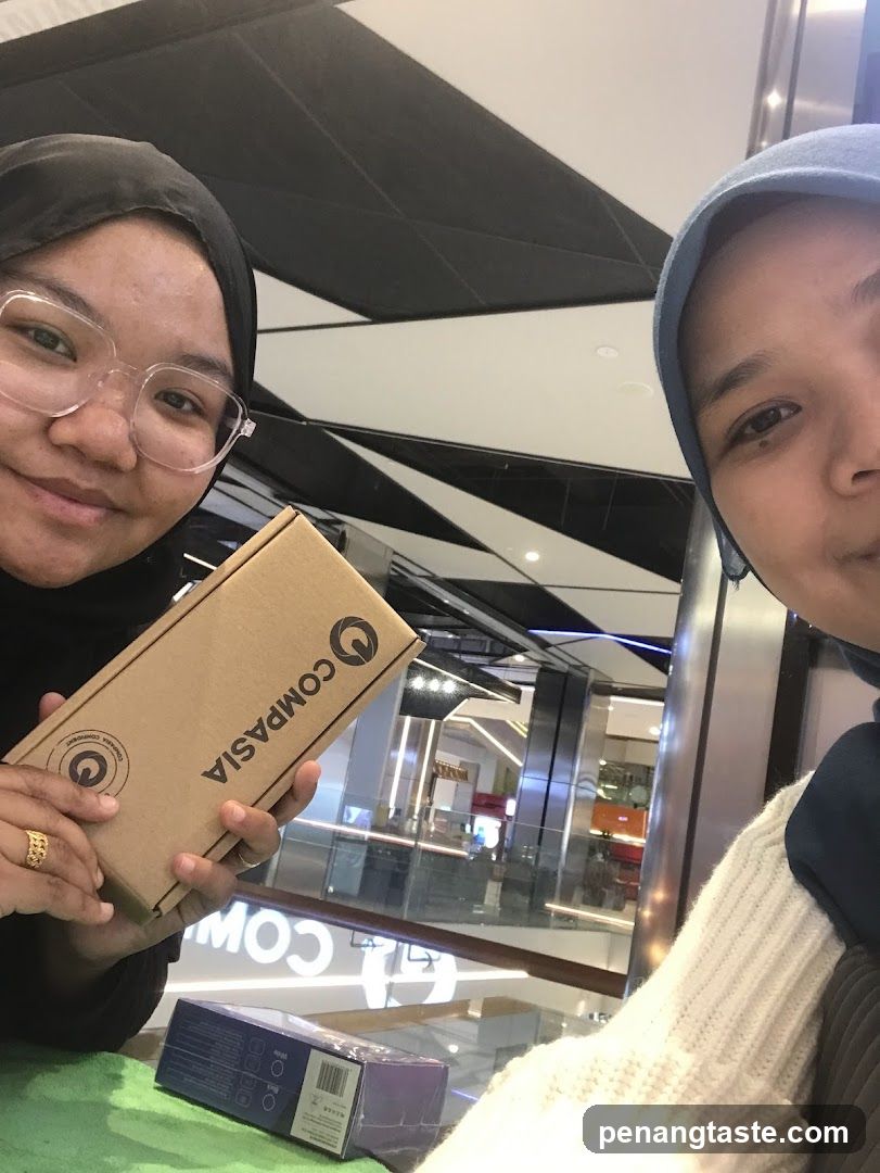 Two individuals in a shopping mall holding a product box