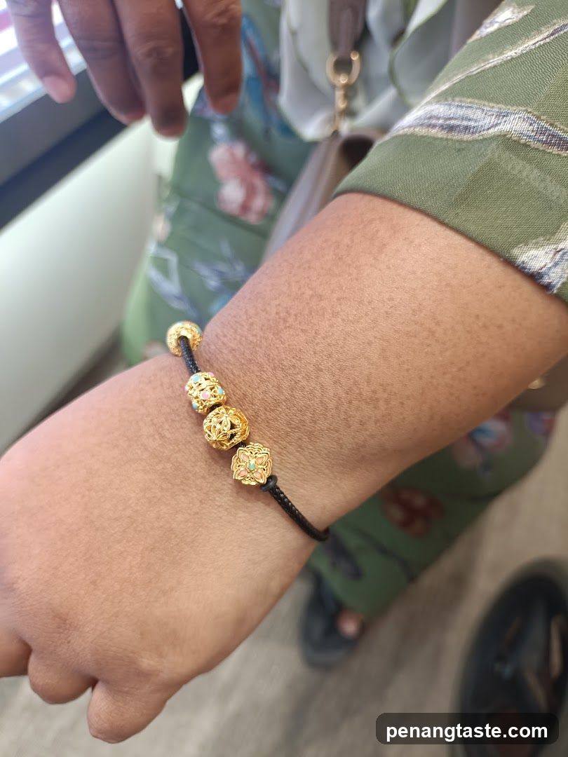 Close-up of a person's wrist with gold charms on a black cord bracelet