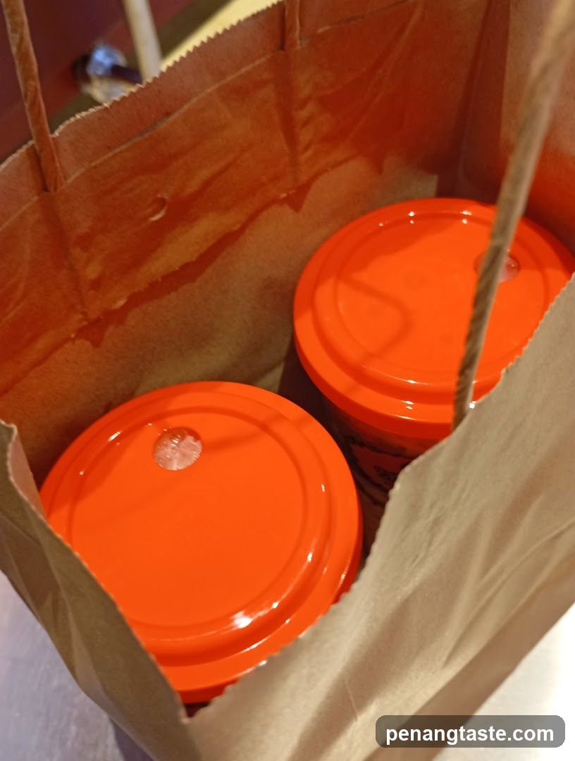 Two orange-lidded cups in a brown paper bag