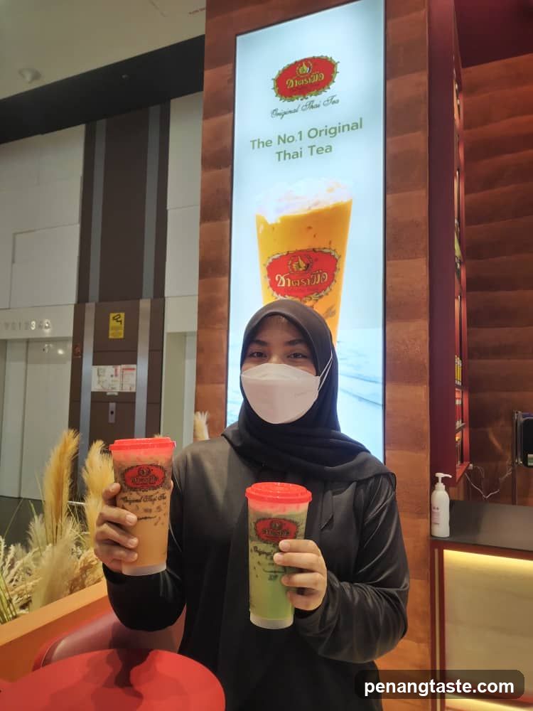 Person holding Thai tea drinks in front of advertisement