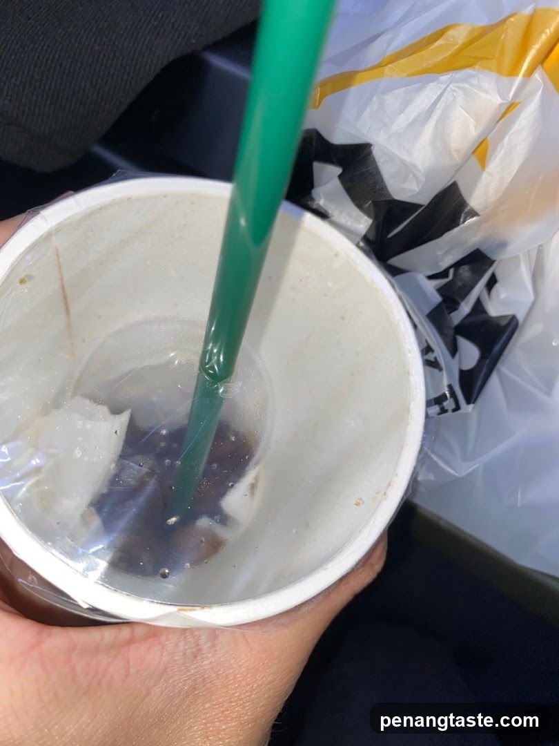 Hand holding a used beverage cup with a green straw