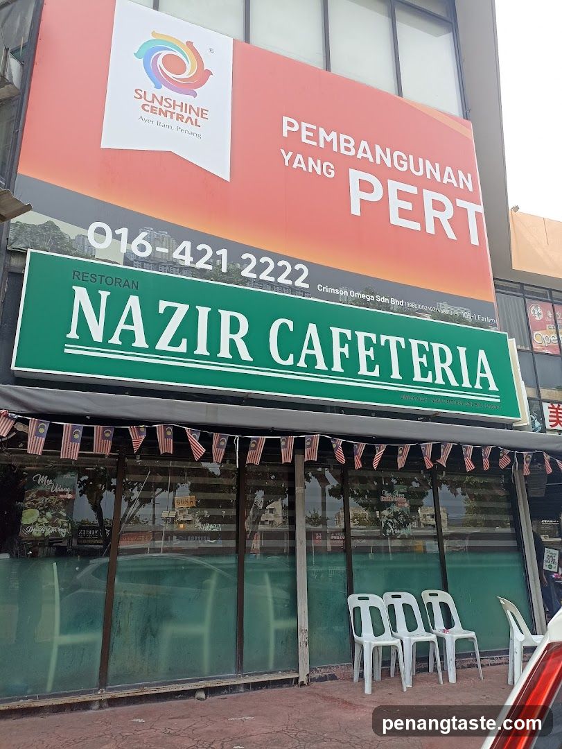 A shop front with a green sign reading 'NAZIR CAFETERIA' and an orange billboard above it displaying 'SUNSHINE CENTRAL' and contact details. The entrance has glass windows adorned with Malaysian flags, and white plastic chairs are placed outside.