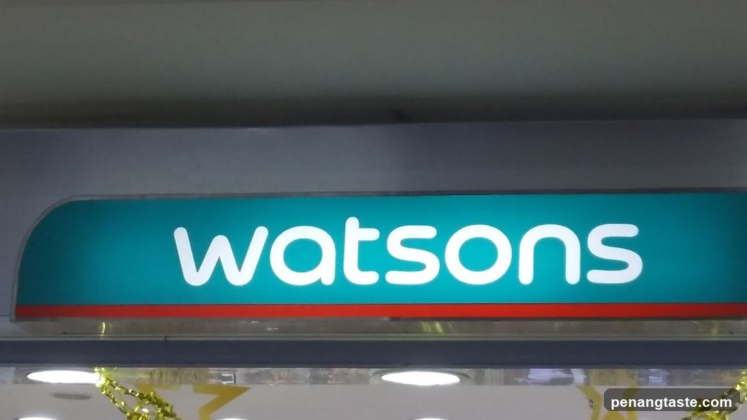 The image shows a close-up of the illuminated 'watsons' sign on the exterior facade of a store, featuring white lowercase lettering against a teal background with a red stripe below.