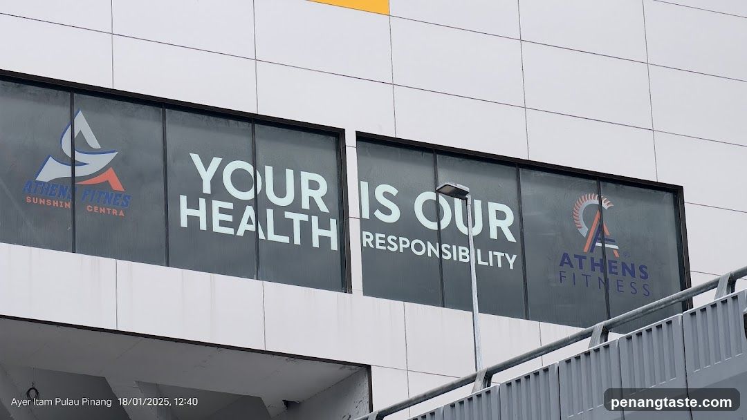 Photo of the exterior facade showing large glass windows with white lettering reading 'YOUR HEALTH IS OUR RESPONSIBILITY'. The Athens Fitness logo appears on both sides of the message, indicating a fitness center entrance or storefront.