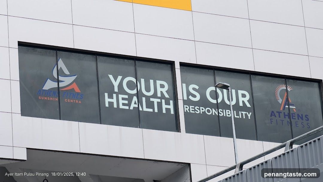 Exterior view of Athens Fitness Sunshine Centra storefront with large glass windows displaying the slogan 'YOUR HEALTH IS OUR RESPONSIBILITY' and branding logos.