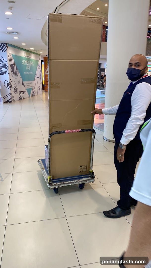 Staff Moving Large Box in Mall Corridor