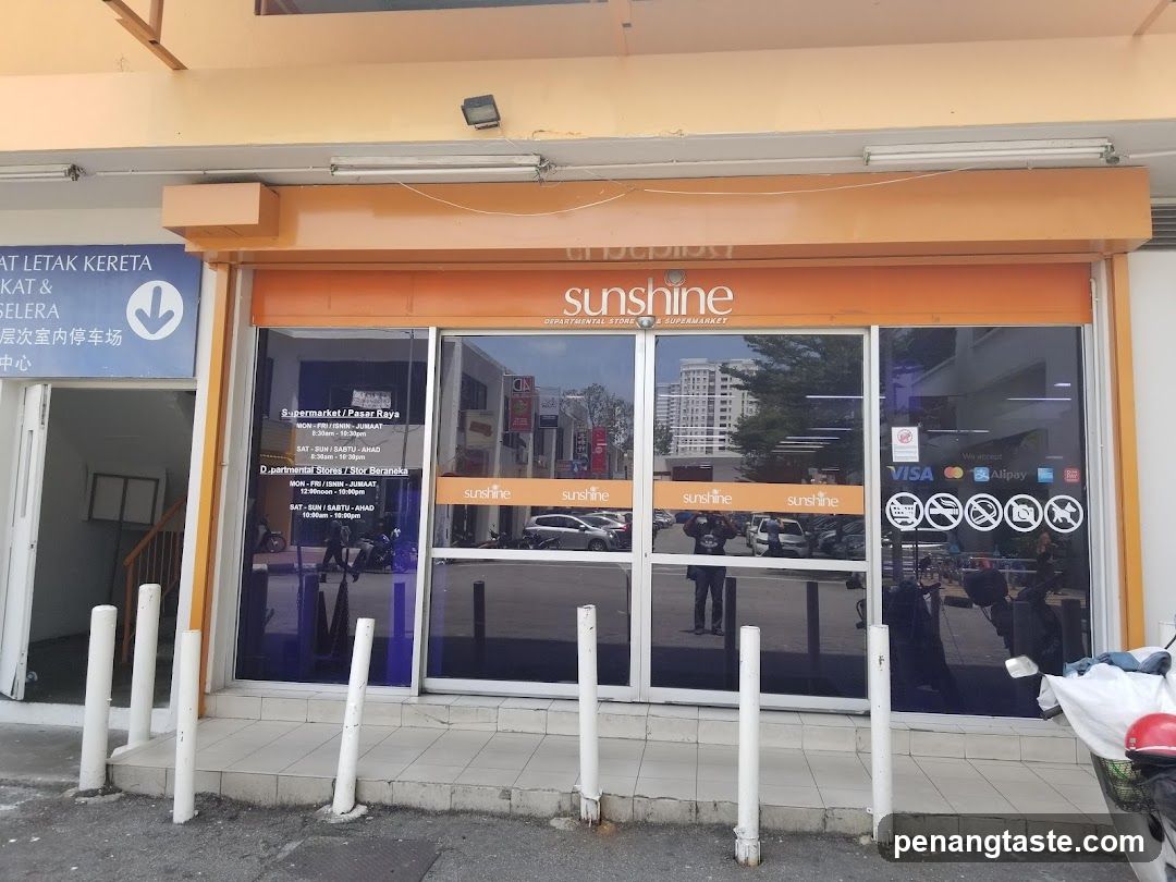 The image shows the storefront of a supermarket named 'sunshine'. The entrance features large glass doors with orange signage displaying the store name and payment logos including Visa, MasterCard, Alipay, and contactless payment symbols. A blue sign to the left indicates parking information in Malay and Chinese. White bollards are placed at the sidewalk edge.