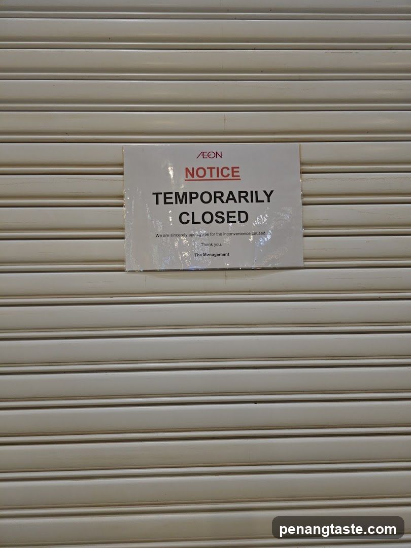 The image shows a closed storefront with horizontal metal shutters. A white notice is affixed to the shutter, displaying 'AEON NOTICE' in red and black text, followed by 'TEMPORARILY CLOSED'. Below this, smaller text reads: 'We are sincerely sorry for the inconvenience caused.' It ends with 'Thank you. The Management', indicating an official closure message from the store's management team.