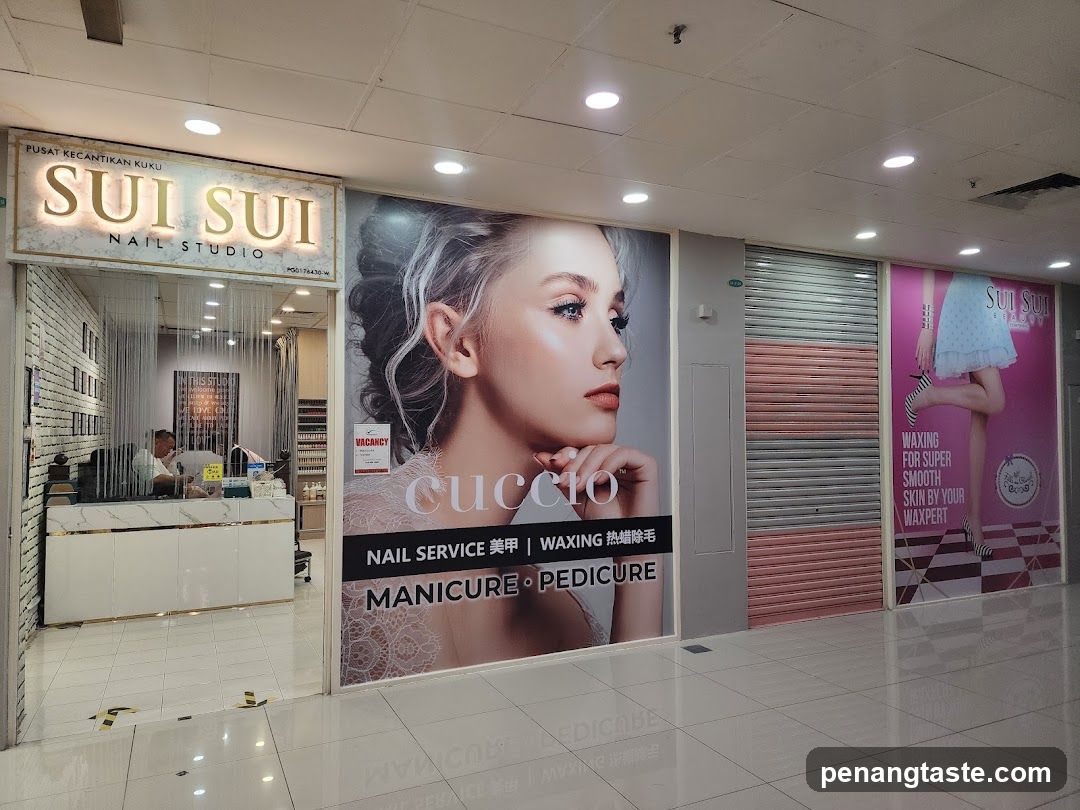A storefront of a nail studio named 'Sui Sui Nail Studio' with visible signage above the entrance. The shop features large posters advertising manicure and pedicure services, including waxing. Inside, there is a reception desk and shelves displaying products.