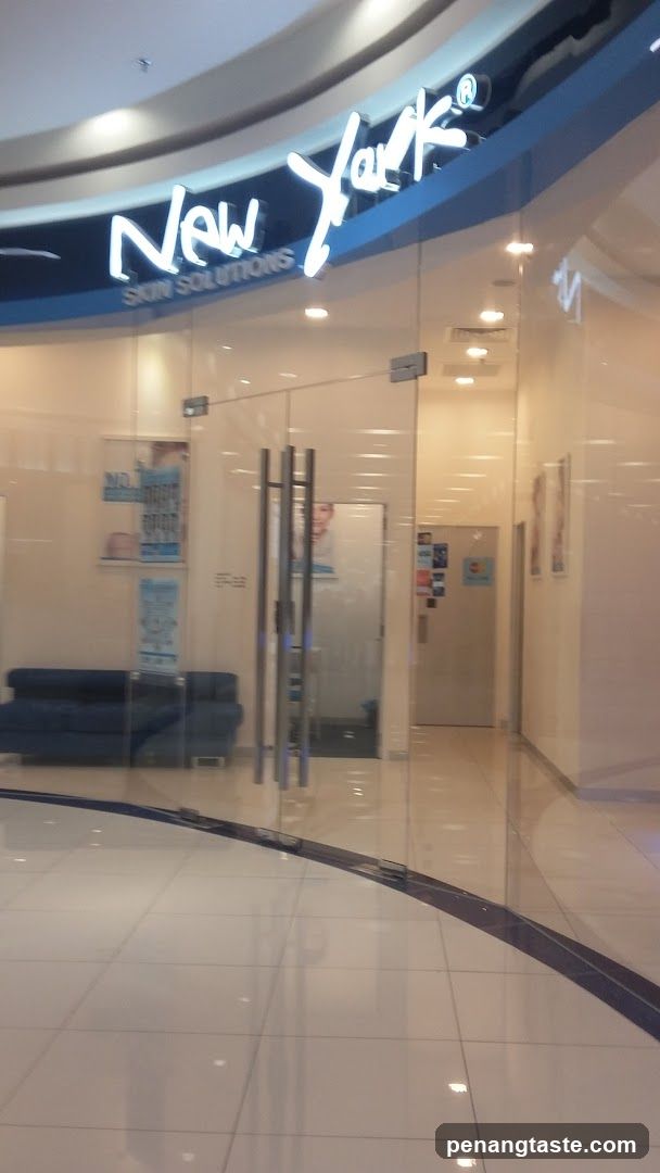 A storefront with a glass entrance and signage reading 'New York Skin Solutions' in illuminated letters above the door. Inside, there is a blue sofa and posters on the walls.