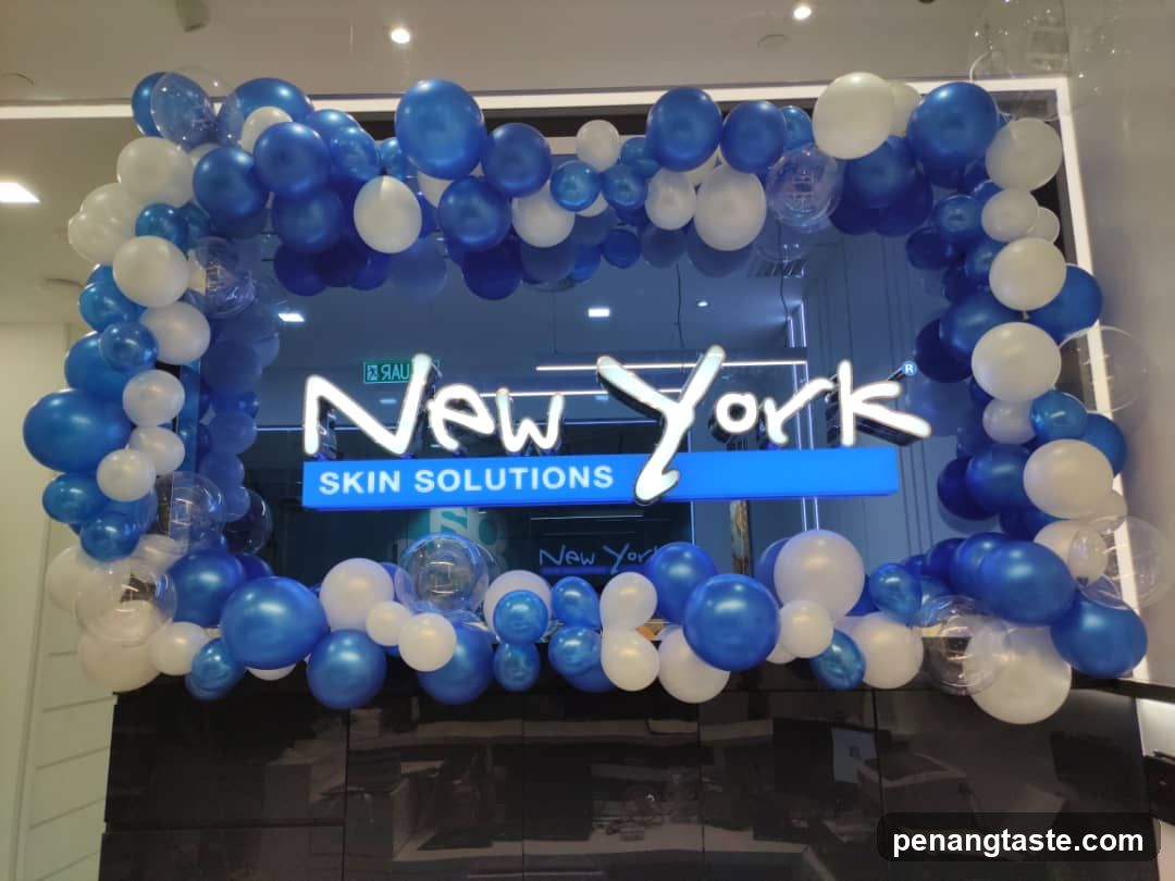A storefront entrance decorated with blue and white balloons forming a rectangular frame around the glass door. The sign reads 'New York' in stylized white lettering, with 'SKIN SOLUTIONS' below it on a blue background. Reflections of interior elements are visible through the glass.