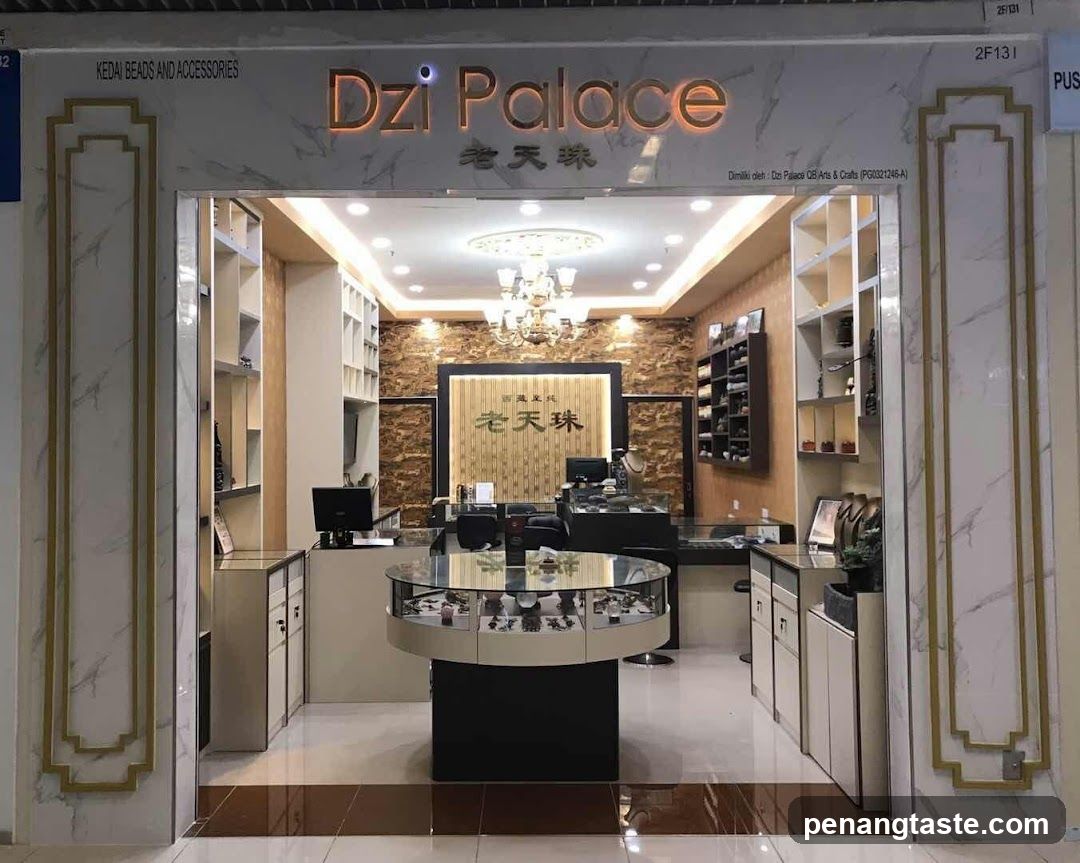 The image shows the storefront of a jewelry shop named 'Dzi Palace' (老天珠). The entrance features a wide, open doorway with marble-like columns on either side, adorned with gold trim. Inside, the store is well-lit with recessed lighting and a chandelier hanging from the ceiling. A central display table showcases various jewelry items, surrounded by shelves filled with products. The back wall has a textured stone design with the shop's name prominently displayed.