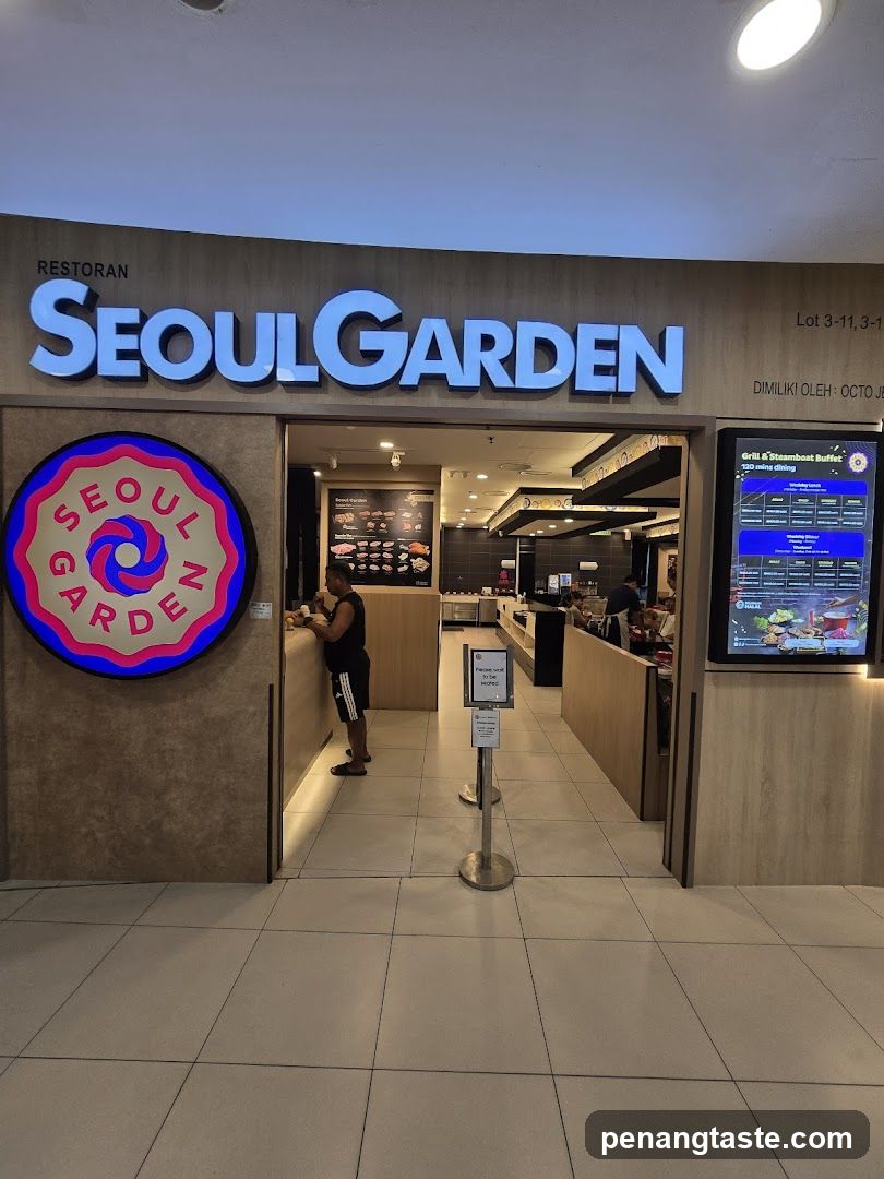 A storefront entrance to Seoul Garden restaurant, featuring a large illuminated sign above the door and a circular logo on the left wall. Inside, customers are visible near the counter area.