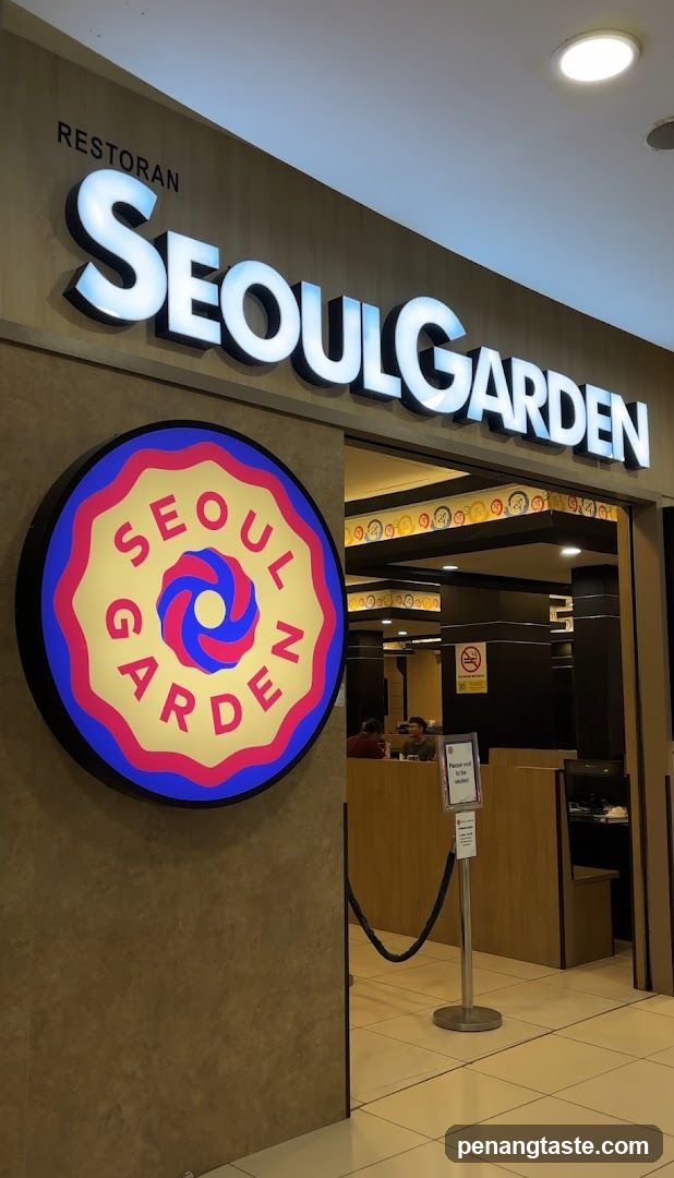 The image shows the storefront of a restaurant named 'SEOULGARDEN'. The sign is prominently displayed above the entrance with large, illuminated letters. Below the main sign, there is a circular logo featuring the words 'SEOUL GARDEN' in red and blue colors. Inside, through the open doorway, you can see part of the interior including wooden counters and seating areas.