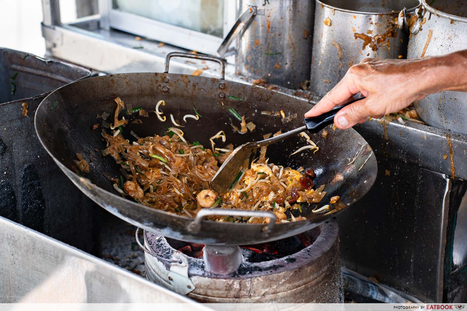 Char kway teow being stir-fried over a charcoal wok at a Penang hawker stall