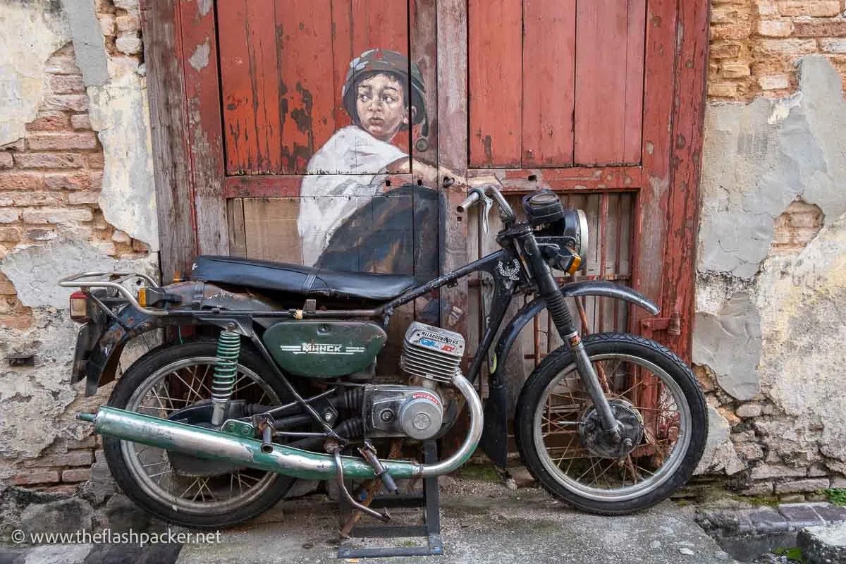 Ernest Zacharevic's Boy on Motorbike mural on Lebuh Ah Quee with a real vintage motorcycle