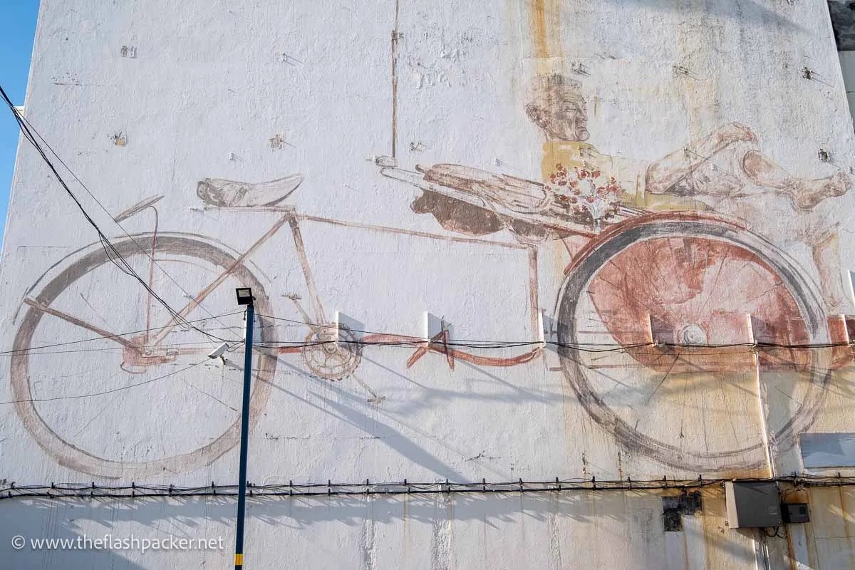 Faded Ernest Zacharevic Trishaw Man mural above Trishaw Corner where drivers congregate in George Town